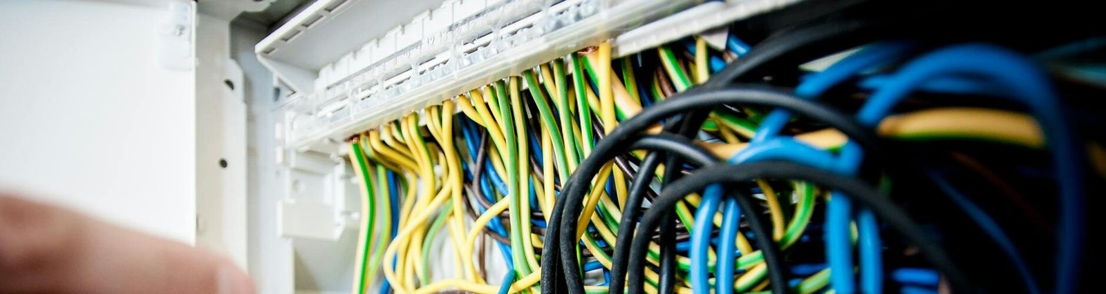 Hand of electrician working on a circuit breaker panel with colorful wires, ensuring safe electrical connections.